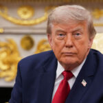 President Donald Trump sits in the Oval Office as he looks towards the camera.