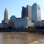 Downtown city skyline of Columbus, Ohio with river and blue sky in the background.
