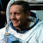 Smiling astronaut in a white spacesuit with an American flag patch on the arm, sitting in front of equipment, preparing for a mission—one of the many unsung heroes ready to push the boundaries of exploration.