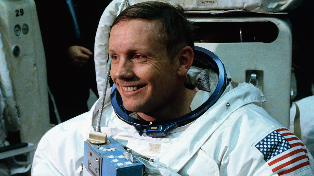 Smiling astronaut in a white spacesuit with an American flag patch on the arm, sitting in front of equipment, preparing for a mission—one of the many unsung heroes ready to push the boundaries of exploration.