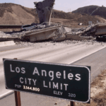 A collapsed freeway overpass blocks a deserted highway near a Los Angeles City Limit sign, with hills in the background and one car parked near the rubble.