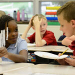 Children in school uniforms smile at each other as they hold white paper plates.