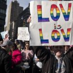 A demonstrater holds up a banner saying "Love Is Love"