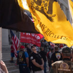 Gun rights activists stand with multiple flags at the Ohio Capitol, with the yellow 'Don't Tread on Me' flag prominently displayed.