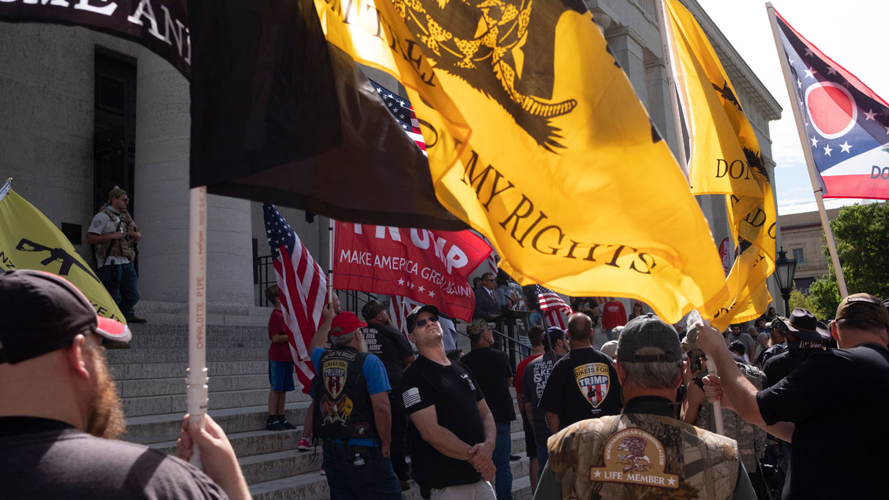 Gun rights activists stand with multiple flags at the Ohio Capitol, with the yellow 'Don't Tread on Me' flag prominently displayed.