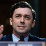 Senator Jon Ossoff appears in a suit and speaks into a microphone, gesturing with his hands during the Senate hearing questioning the Director of National Intelligence nominee Jay Clayton.