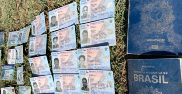 Multiple Brazilian ID cards and two dark blue Brazilian passports are laid out on grass, partially overlapping each other. The documents display photos, text, and official emblems.