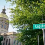 The Georgia State Capitol building is featured with trees and a street sign that says Capitol Square SW.