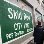 Green sign with white lettering reading "Skid Row City Limit. Pop Too Many."
