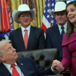 Donald Trump holds hands with Rep. Elise Stefanik (R-NY) in the Oval Office with other officials gathered around.