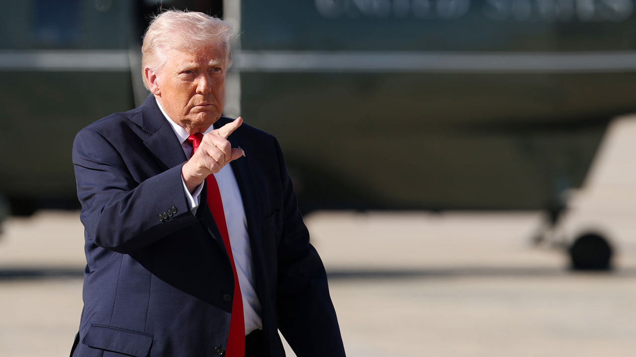 President Donald Trump points ahead of him with Air Force One in the background.