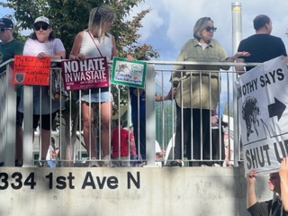 Why These Women Rallied for Sophie Cunningham in Seattle 2 A group of people stand behind a metal railing holding protest signs, including messages like No Hate in Wausau and Shut Up. Among the crowd at 334 1st Ave N, one sign references Sophie Cunningham, highlighting solidarity and community values.
