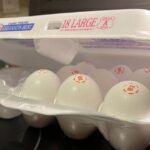 A carton of large eggs rests on a kitchen stove.