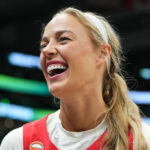 Sophie Cunningham, in red basketball jersey with white t-shirt, with a beaming smile.