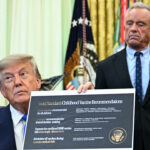 A man in a suit holds up a document titled Gold Standard Childhood Vaccine Recommendations while another man stands behind him in an official-looking room with flags in the background.